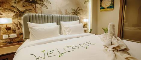 A hotel room with a bed, a headboard, a nightstand, a lamp, a painting, and a towel on the bed.