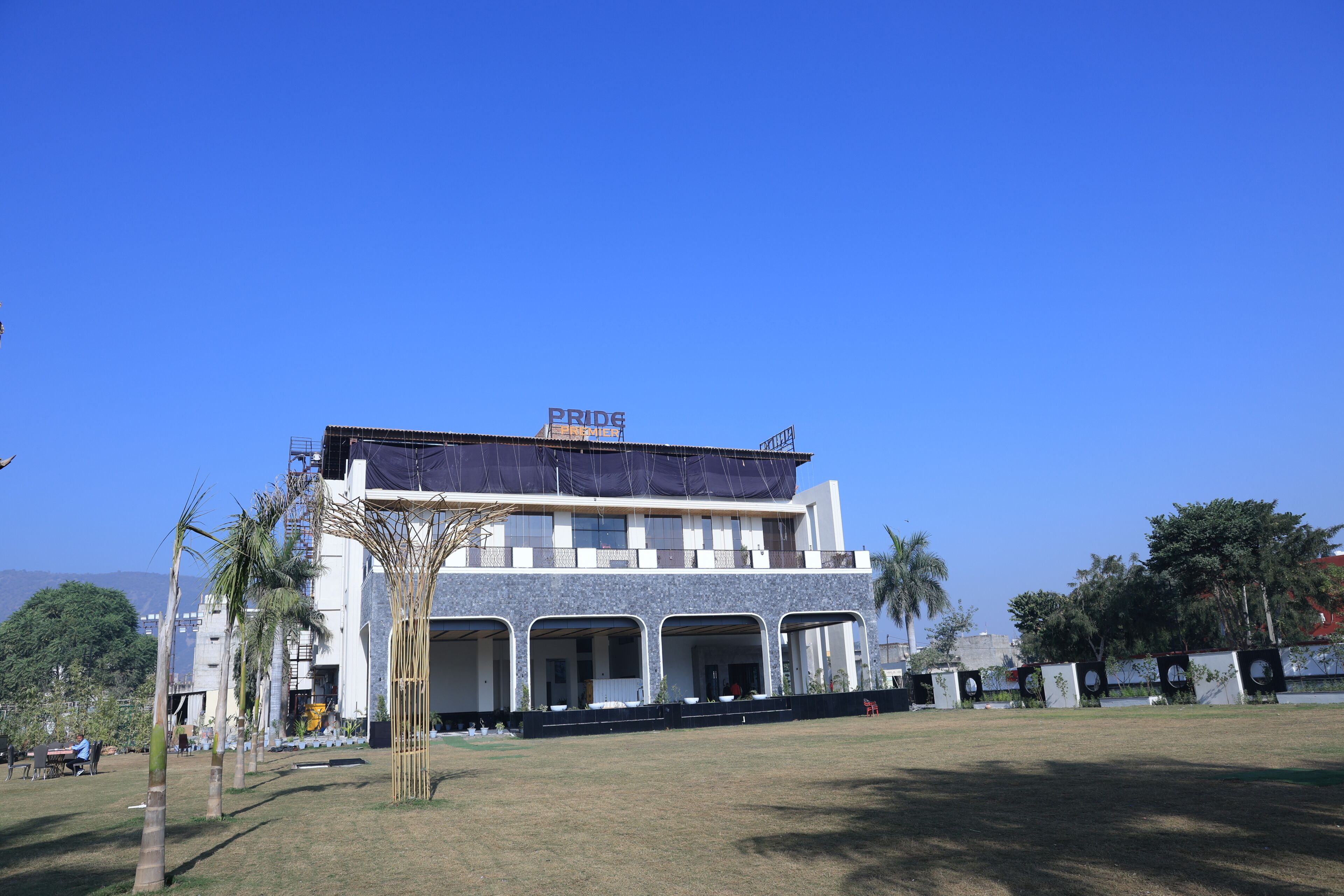 A modern building with a covered entrance, a sign reading 'PRIDE,' and a grassy area in front.