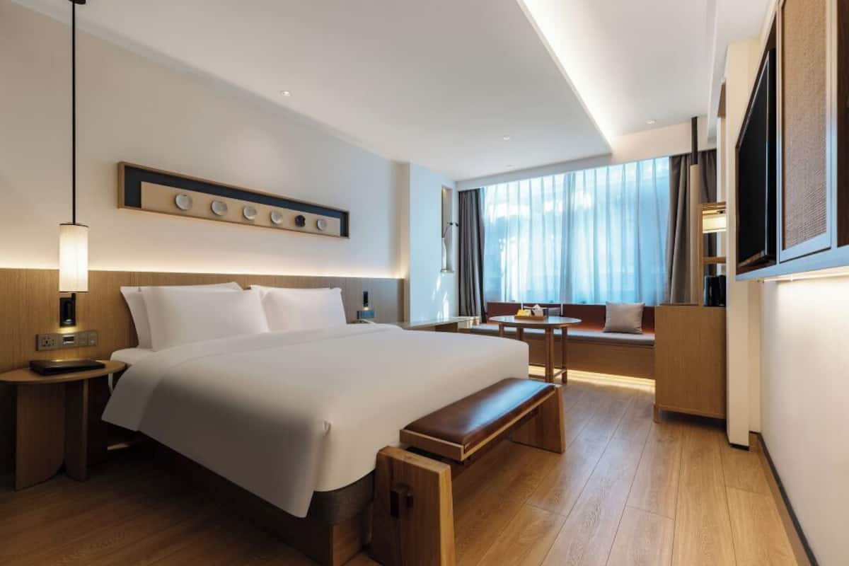 Habitación de hotel moderna con una cama grande, mesitas de noche, un banco, una pequeña mesa y un televisor.