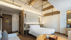 A modern hotel room with a large bed, a sofa, a wooden table with a cup and box, and pendant lighting. - E Hotel-Kuanzhai Alley (Chengdu)