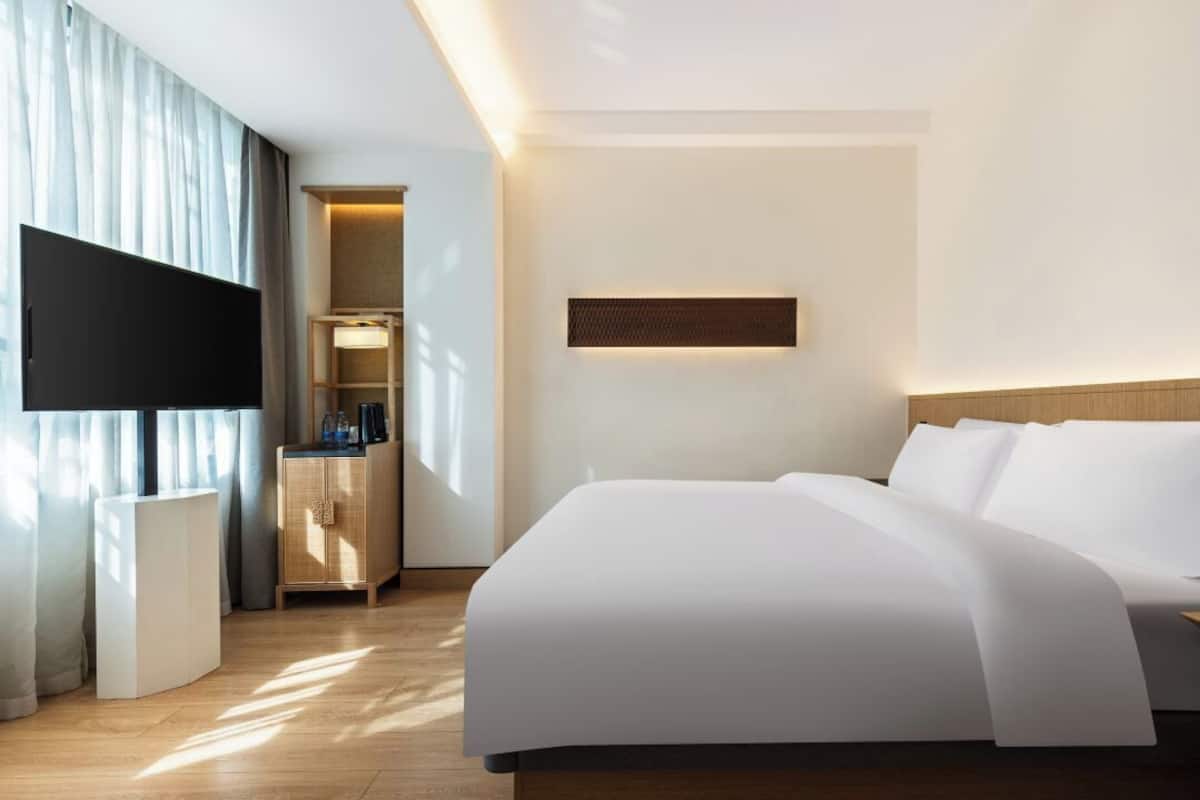 Una habitación de hotel con una cama grande, un televisor de pantalla plana montado en la pared, una mesita de noche y un armario pequeño.