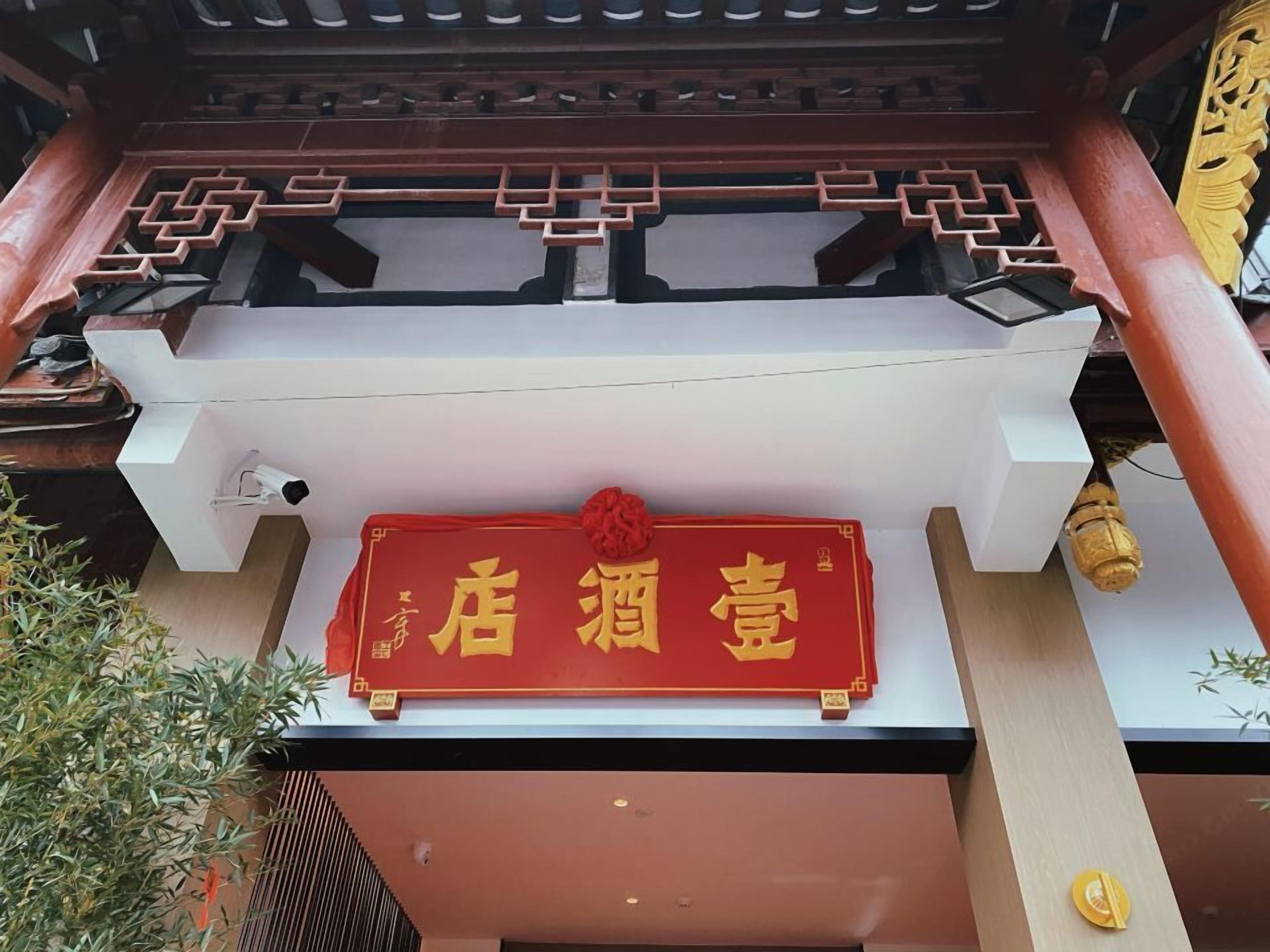 Een rood bord met gouden Chinese karakters op de gevel van een gebouw.