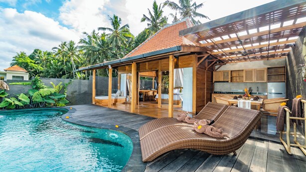 A poolside area with a lounge chair, a covered seating area, and a kitchen visible through an open door. - Aix di Sawah Ubud (Tegallalang)
