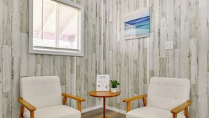 A room with two white upholstered chairs, a small wooden table with a welcome sign and a potted plant, and a window with blinds. - Near Dtwn & Space Center: Tiny Home in Picayune (Picayune)