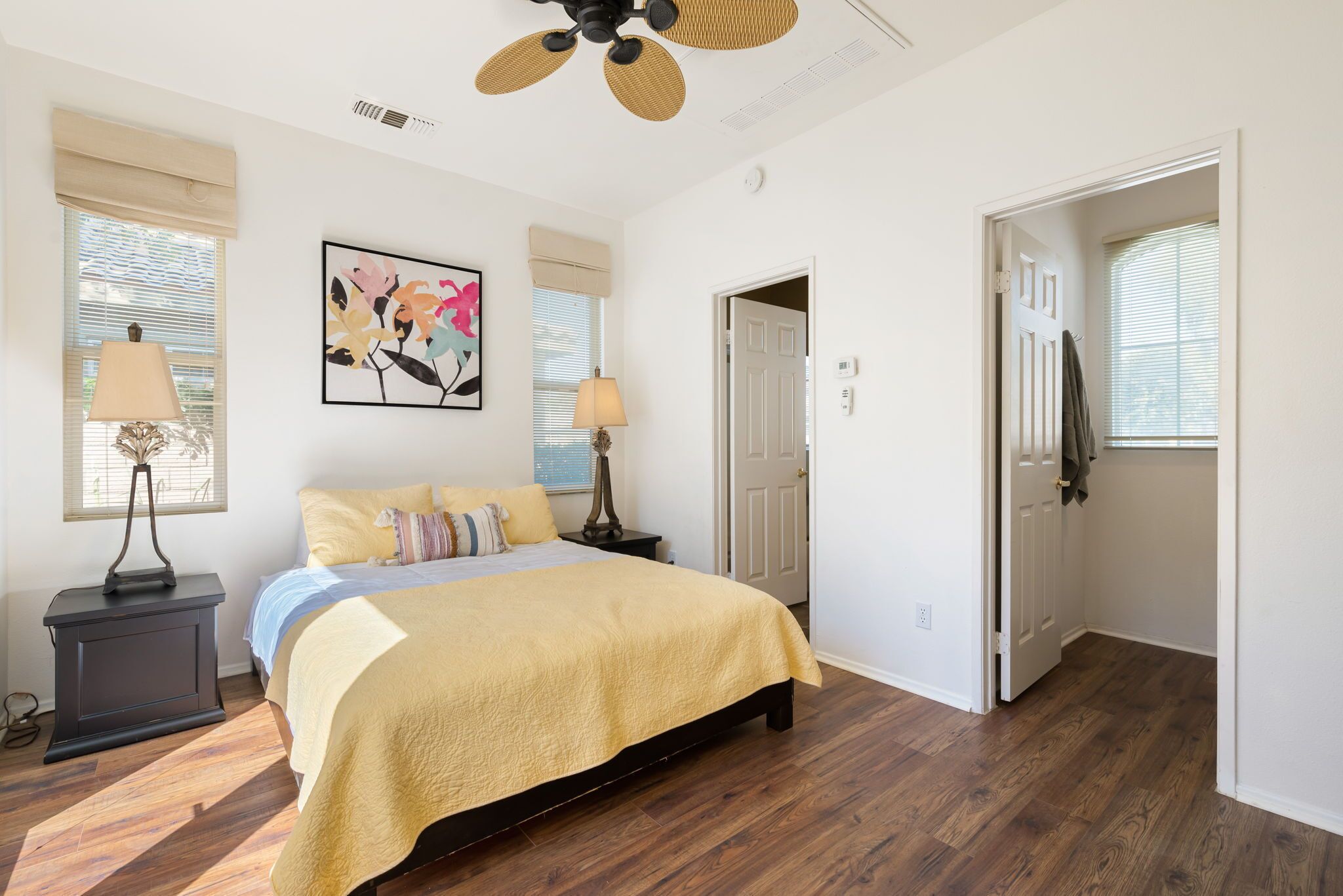 A bedroom with a bed, two bedside tables, a ceiling fan, and a door leading to another room.