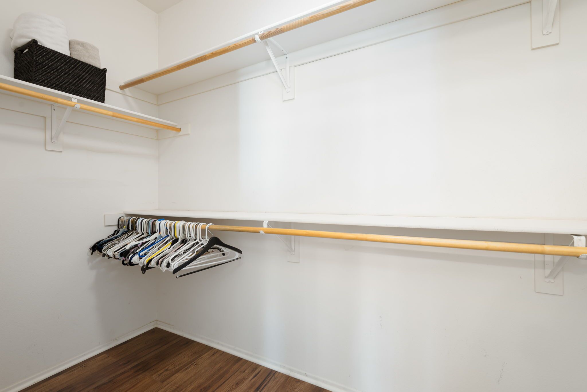 Ein begehbarer Kleiderschrank mit Holzstangen zum Aufhängen von Kleidung und einem Regal mit gefalteter Kleidung.