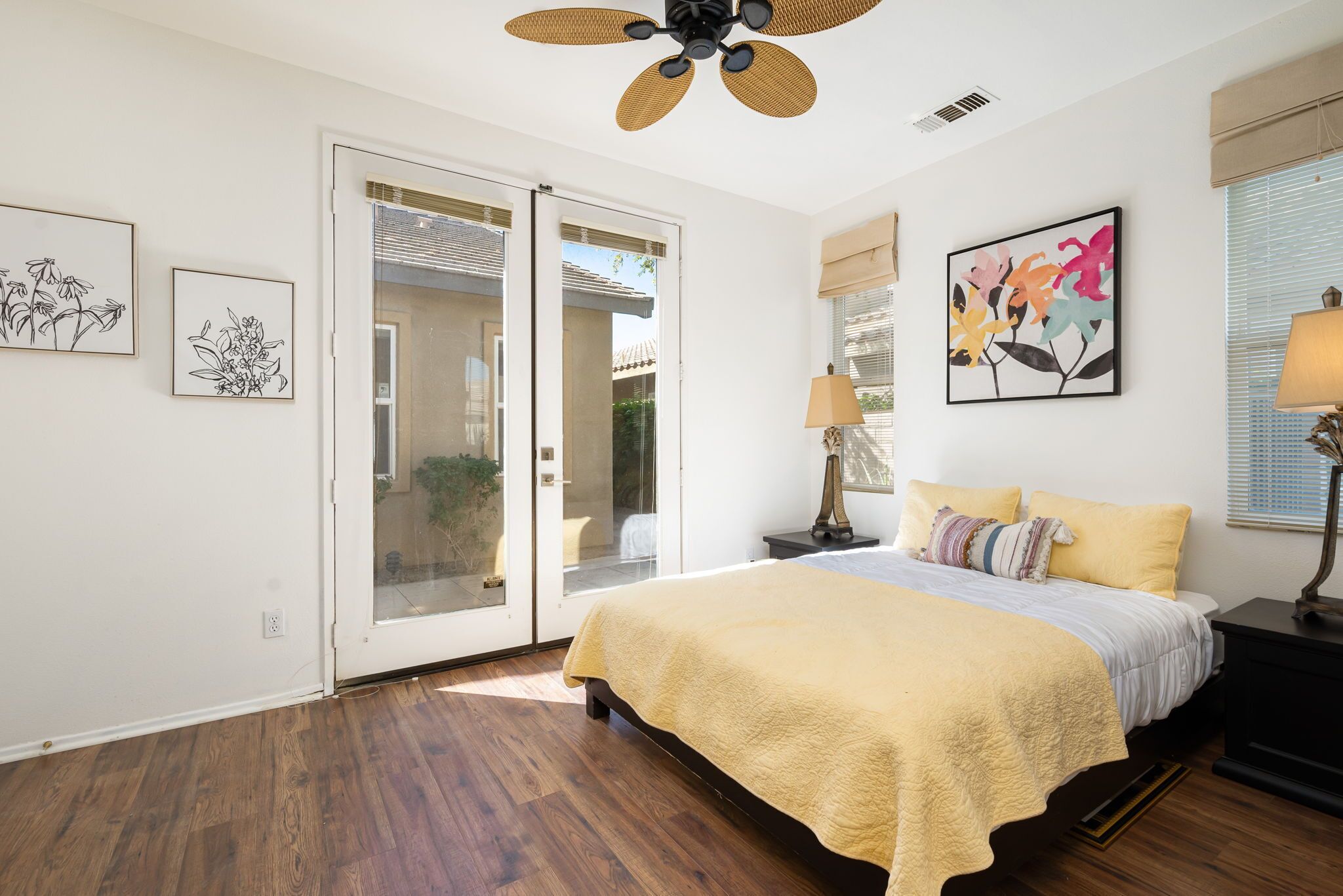 A bedroom with a bed, a ceiling fan, a door leading to a balcony, and artwork on the walls.