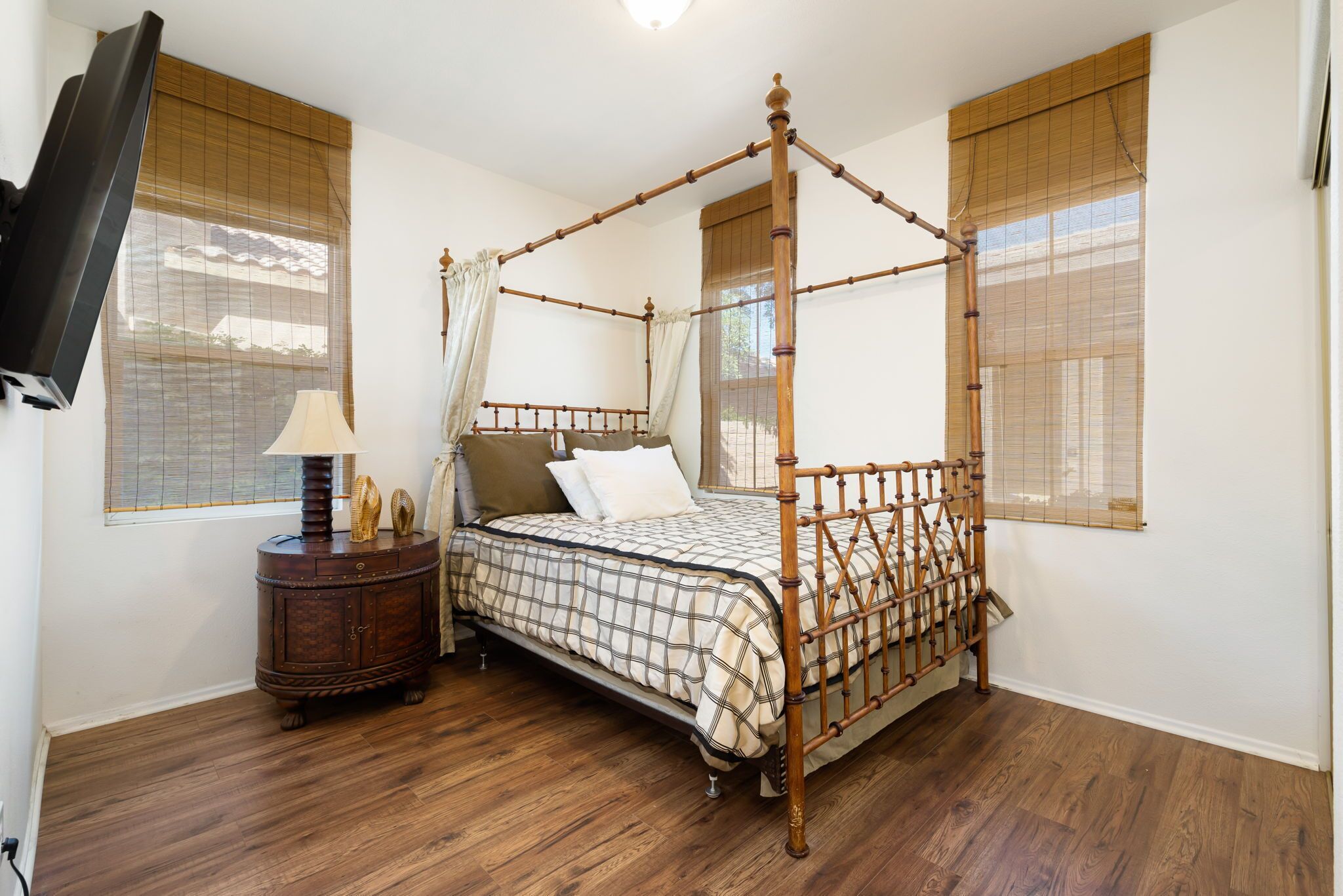 A four-poster bed with a checkered bedspread, a bedside table with a lamp, and a television mounted on the wall.
