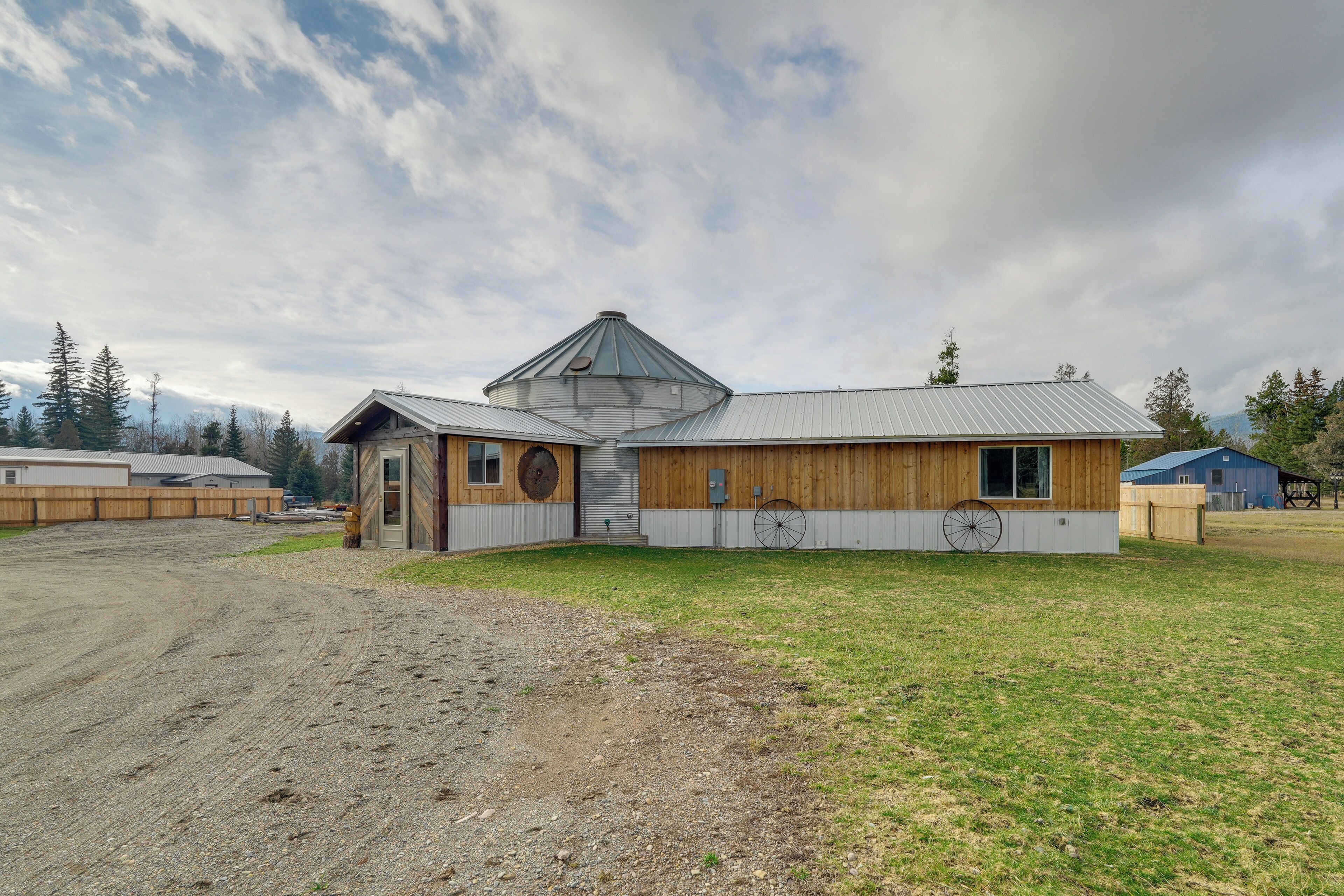 A wooden building with a silo, a wheel, and a barn in the background.