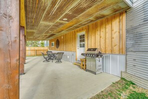 Eine Terrasse im Freien mit Grill, Sitzgelegenheit und einem Holzzaun im Hintergrund.