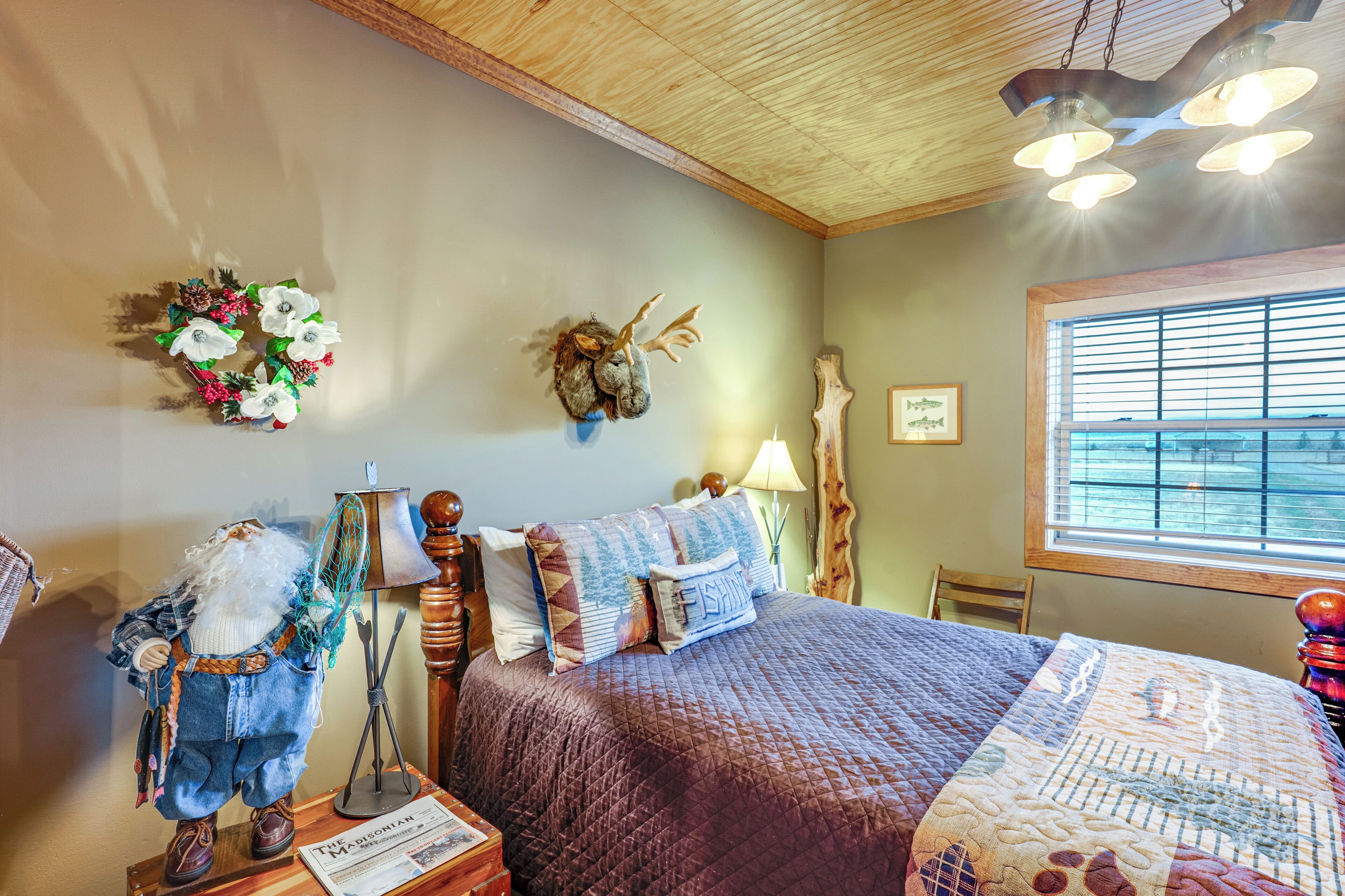 A bedroom with a large bed, a wooden ceiling, a window with blinds, and a wall decoration.