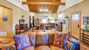 A spacious living area with a leather sofa, wooden ceiling beams, and a kitchen in the background. - Ennis Home: Try the Yellowstone Lifestyle! (Ennis)