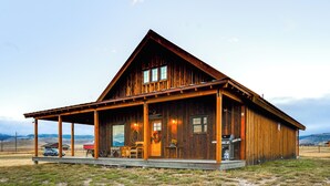 A wooden cabin with a porch, a barbecue grill, and a car parked outside. - Ennis Home: Try the Yellowstone Lifestyle! (Ennis)