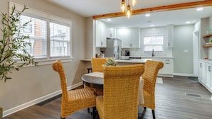 A modern kitchen with white cabinets, a stainless steel refrigerator, and a dining area with wicker chairs and a round table. - Walk to Downtown Frankfort: Patio, Firepit & More! (Frankfort)