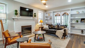 A living room with a fireplace, a ceiling fan, a TV mounted on the wall, and a bookshelf. - Walk to Downtown Frankfort: Patio, Firepit & More! (Frankfort)