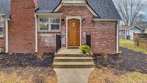 A brick house with a wooden front door, a small porch, and a concrete pathway leading to the door. - Walk to Downtown Frankfort: Patio, Firepit & More! (Frankfort)