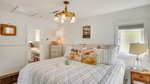 Quarto com cama, mesa de cabeceira, luminária, cômoda e janela com persianas.