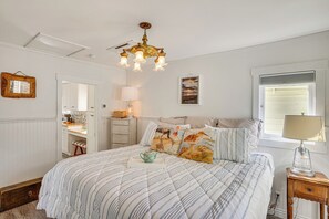 A bedroom with a bed, a bedside table, a lamp, a dresser, and a window with blinds. - Remodeled, AC, Walk to the Beach - Guest Favorite! (Avalon)