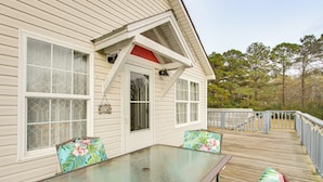 A wooden deck with a glass table and chairs, a covered area with a red roof, and a view of trees. - Near Tennessee River! Pet-Friendly Family Cottage! (Savannah)