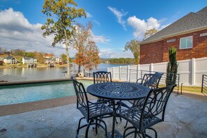 Eine Terrasse mit Pool, Gartenmöbeln und Blick auf einen See sowie Häuser im Hintergrund.