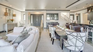 A spacious living room with a large white sofa, a dining area with a wooden table and modern chairs, and a kitchen in the background. - Private Pool & Slip: Luxury Lake Hamilton Home! (Hot Springs)