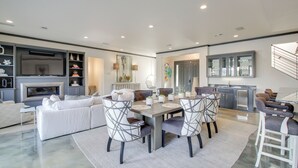 A spacious living room with a large white sofa, a dining table with chairs, and a kitchen area with cabinets and a refrigerator. - Private Pool & Slip: Luxury Lake Hamilton Home! (Hot Springs)