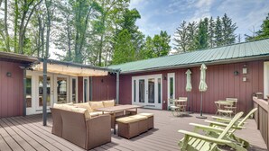 En overdækket terrasse med udendørs møbler, en pergola og udsigt til den omkringliggende skov.