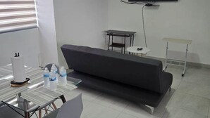 Moderni huone, jossa on sohva, ruokapöytä tuoleineen, pieni valkoinen pöytä ja seinälle asennettu televisio.