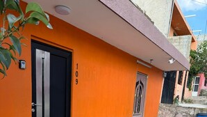 En byggnad med en orange fasad, en svart dörr och en liten blå soptunna.