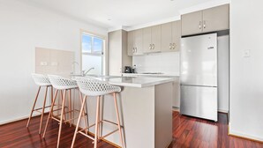 Una cocina moderna con un refrigerador de acero inoxidable, taburetes de bar blancos y piso de madera.