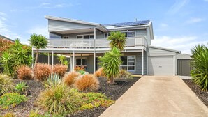 Una casa de dos pisos con balcón, paneles solares y diversas plantas desérticas.
