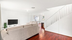 Una sala de estar moderna con un televisor de pantalla plana, un sofá color beige y una escalera con barandillas blancas.