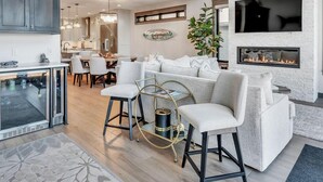 A spacious living area with a high ceiling, a modern chandelier, a fireplace, and a television mounted on the wall. - Lower Gar Family Fun- Private Dock, 6 bedrooms, Close to boat Ramp (Arnolds Park)