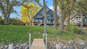 A modern house with a wooden deck leading to a stone pathway. - Lower Gar Family Fun- Private Dock, 6 bedrooms, Close to boat Ramp (Arnolds Park)