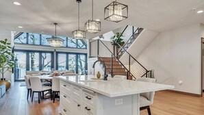 A modern kitchen with a large island, pendant lights, and a staircase leading to an upper level. - Lower Gar Family Fun- Private Dock, 6 bedrooms, Close to boat Ramp (Arnolds Park)
