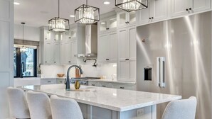 A modern kitchen with white cabinetry, a large island with bar stools, stainless steel appliances, and pendant lighting. - Lower Gar Family Fun- Private Dock, 6 bedrooms, Close to boat Ramp (Arnolds Park)