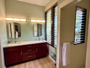 Un baño con un tocador espacioso, dos lavamanos, un espejo y una ventana con persianas.