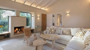 Een moderne woonkamer met een open haard, een zithoek, een eettafel en een groot raam met uitzicht op groen.