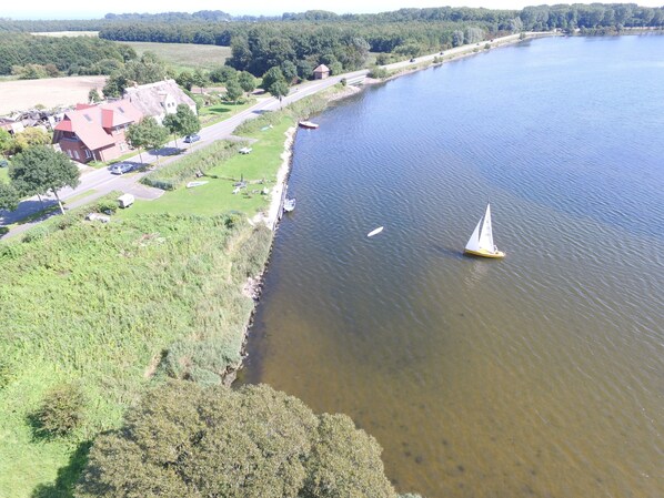 Ein Fluss mit einem Segelboot, eine Straße mit Fahrzeugen und Gebäude entlang des Ufers.
