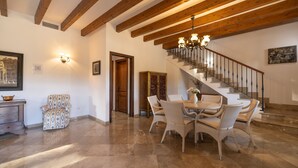 Un vaste espace de vie doté d’un sol en marbre, d’une table à manger avec des chaises en osier, d’un escalier avec une rampe en bois et d’un lustre.