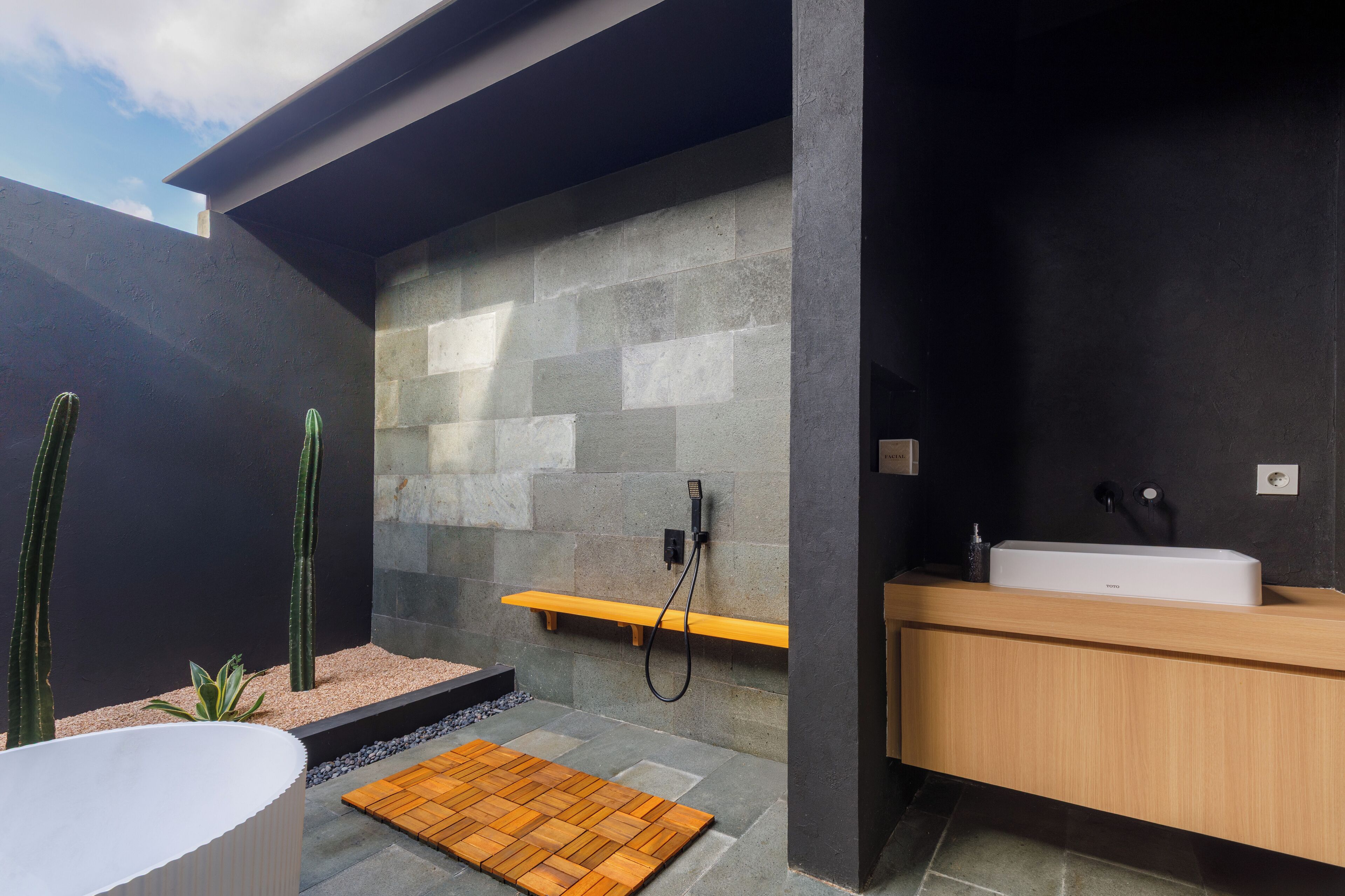 A modern bathroom with a stone wall, a wooden bench, a bathtub, and a sink.