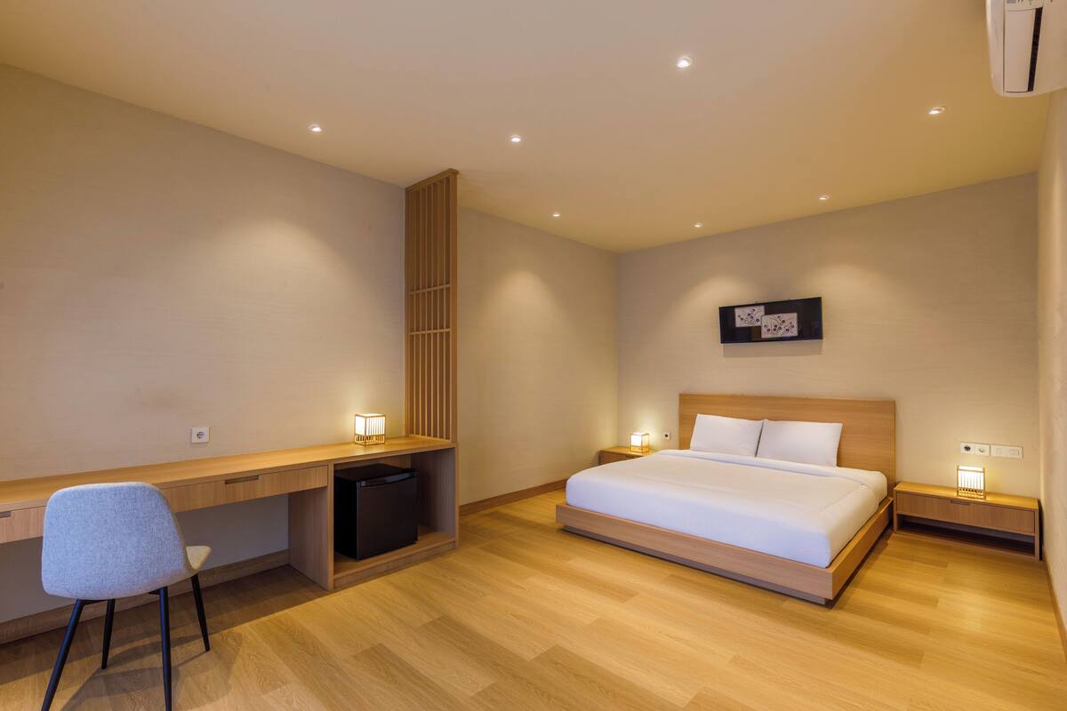 A modern hotel room with a wooden desk, a single bed, and a small bedside table.