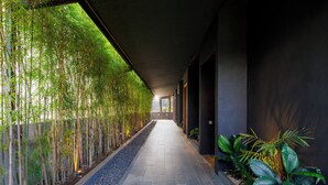 A corridor with a bamboo garden on one side and a dark wall on the other. - Himawari House (Blahbatuh)