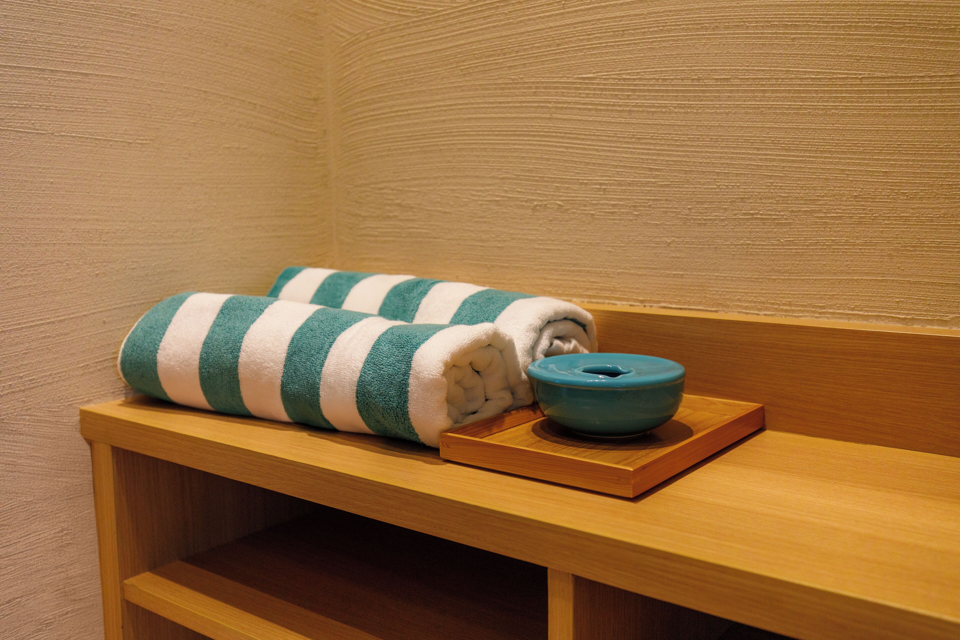 A wooden bench with a rolled towel and a blue bowl on it.