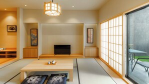 A traditional Japanese-style living room with tatami flooring, a low wooden table, a television, and sliding shoji screens. - Himawari House (Blahbatuh)