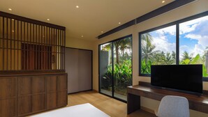 A modern bedroom with a large bed, a desk with a TV, and a sliding glass door leading to a garden. - Himawari House (Blahbatuh)