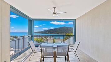 Un balcon avec une table et des chaises, un ventilateur de plafond et une vue sur un lac et des montagnes.