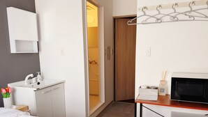 A hotel room with a bed, a desk with a microwave, a small cabinet, a bathroom with a shower, and a wooden door. - AOMUGI RYOKAN (Tokyo)