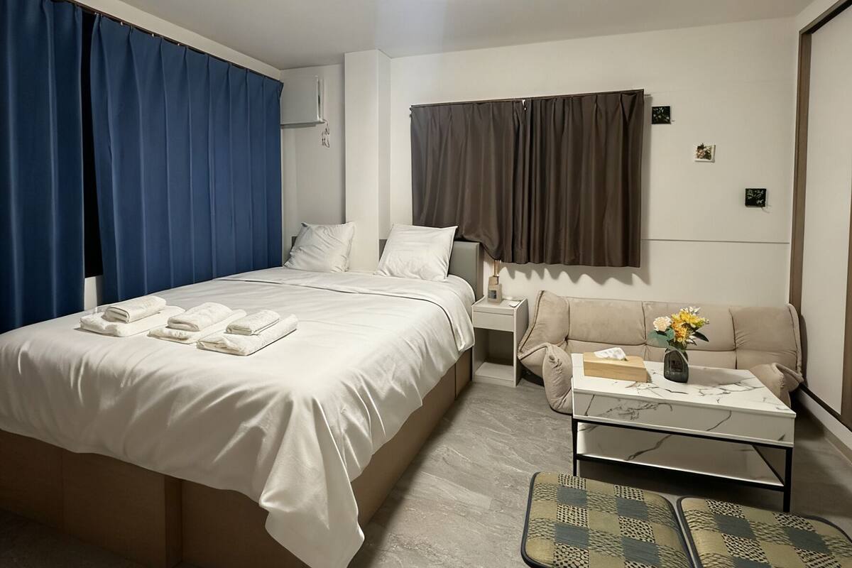 A modern hotel room with a large bed, a sofa, a coffee table, and a small side table.