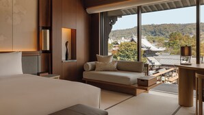 A modern hotel room with a large bed, a sofa, a desk, and a view of traditional architecture. - Capella Kyoto (Kyoto)